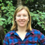 Staff member Nikki Valentine stands in front of green leaves