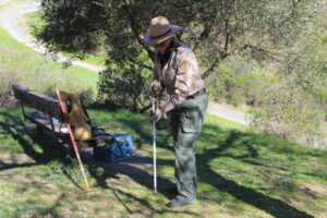 A woman in work clothes and a hat demonstrates the use of a flame torch to kill weed seedlings on damp ground