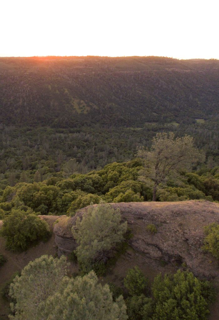 Sunset at Big chico creek with brown rocks in foreground and rolling green brown hills in distance